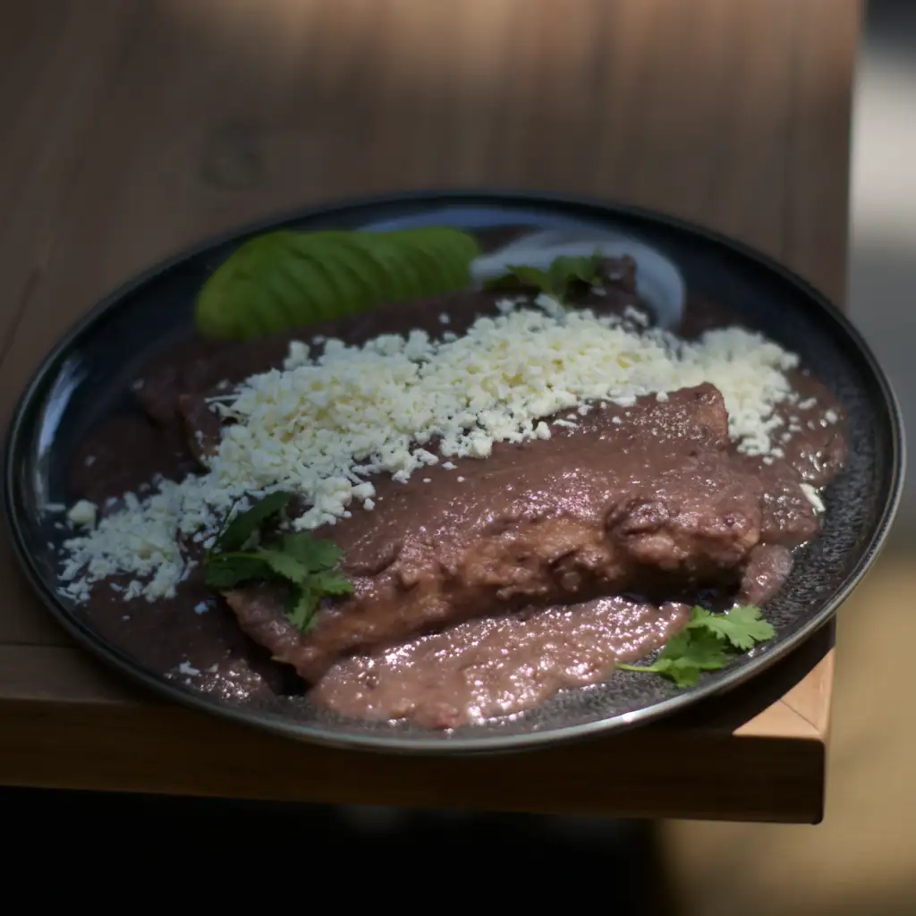 Enfrijoladas de pollo bañadas en frijol negro con cotija y aguacate